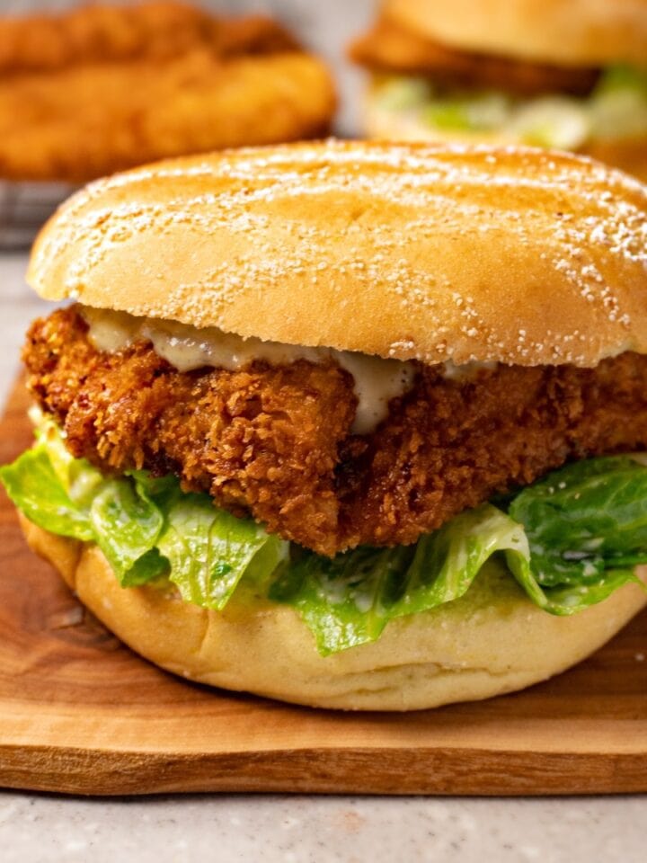 A sandwich with crispy chicken, salad, and white sauce on a wooden board.