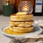 A stack of pancakes topped with a pat of butter and drizzled with maple syrup.
