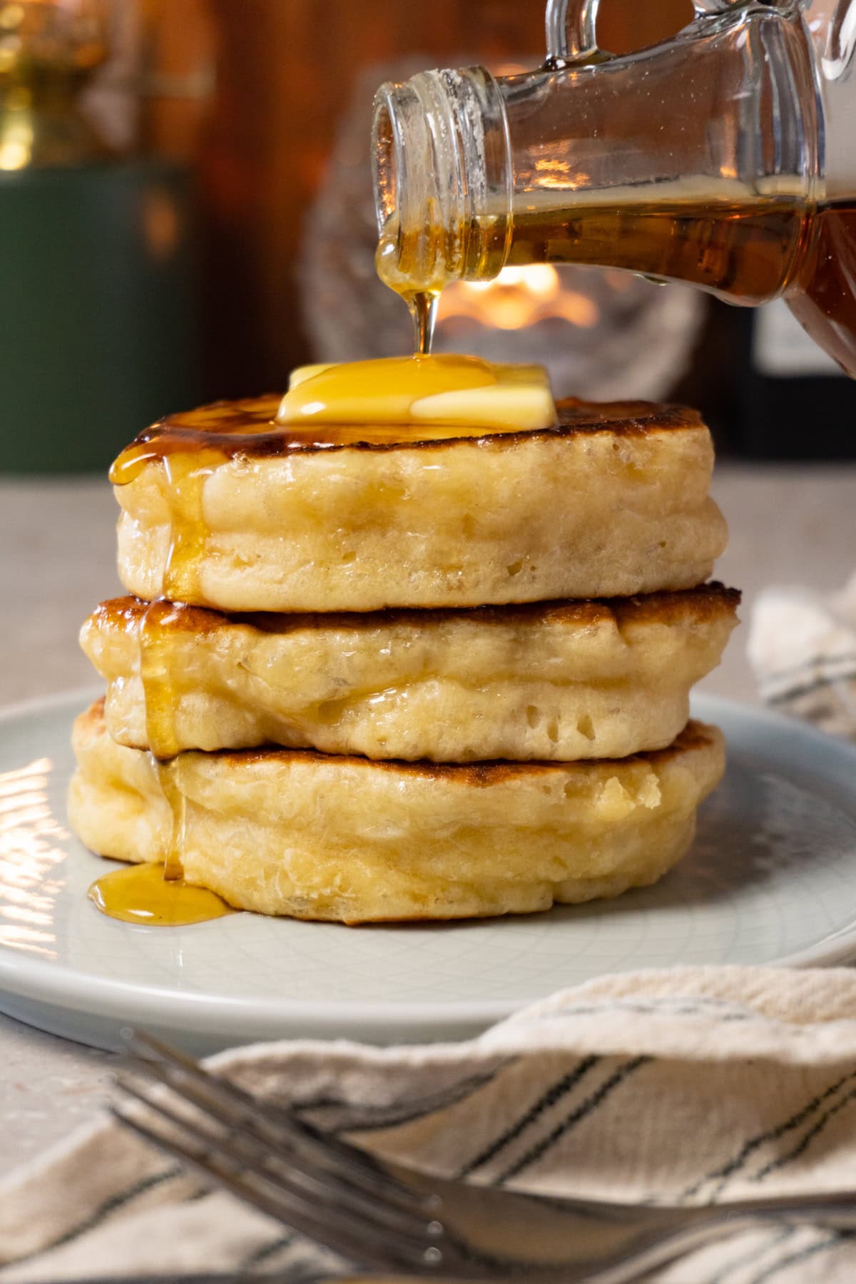 A stack of pancakes topped with a piece of butter, with a bottle pouring maple syrup over them.