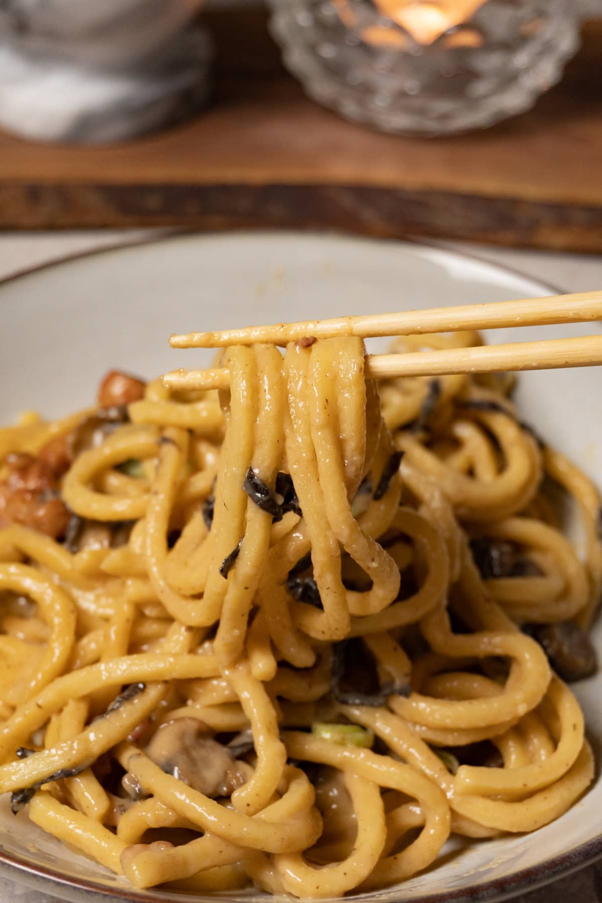 Chopsticks are holding udon noodles in creamy sauce.