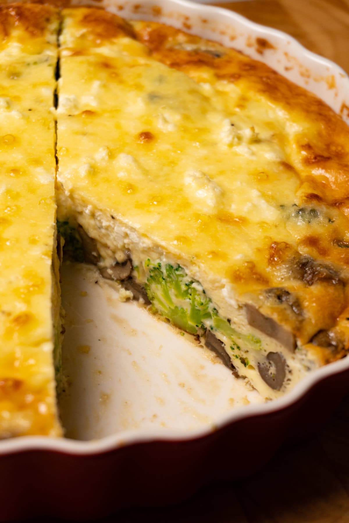 Quiche with broccoli, mushrooms and cheese in a pie dish, with one slice removed.
