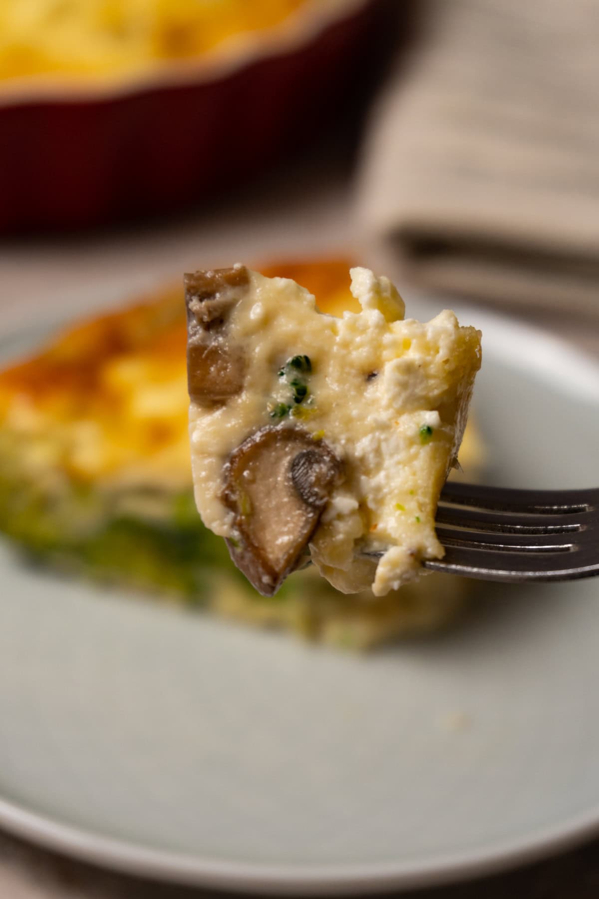 A fork with a piece of quiche with broccoli, mushrooms and cheese.