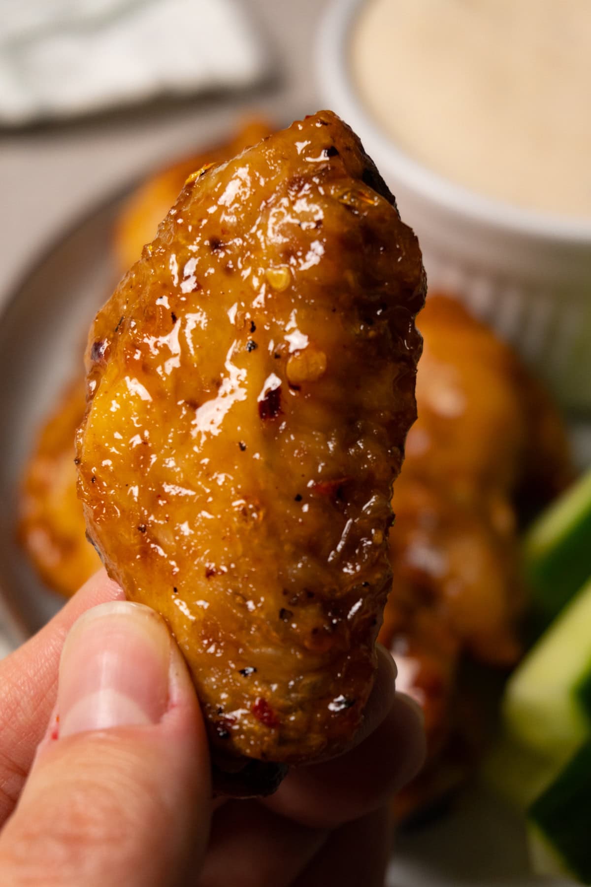A hand is holding a chicken wing flat covered in shiny sauce.