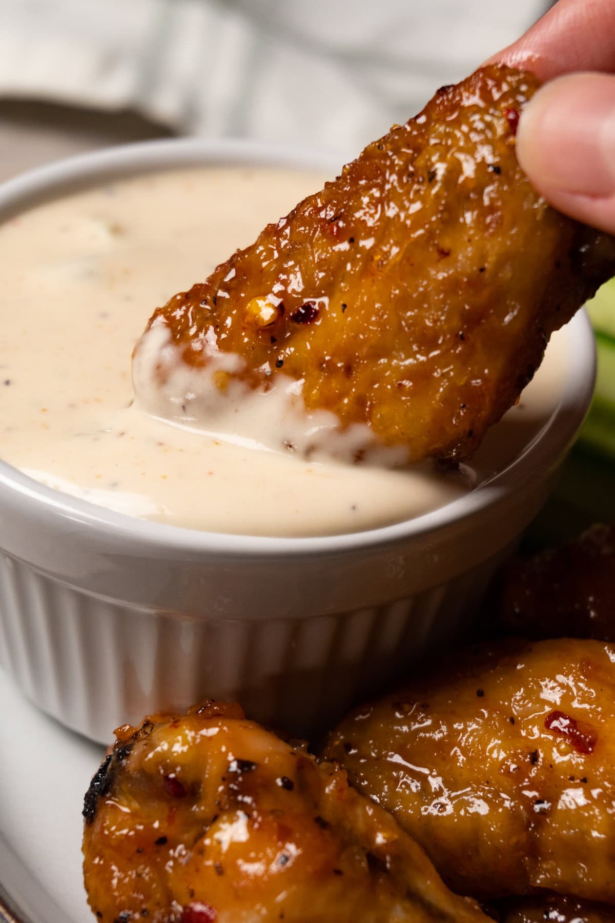 A hand is holding a chicken wing flat and dipping it into white sauce in a white bowl.
