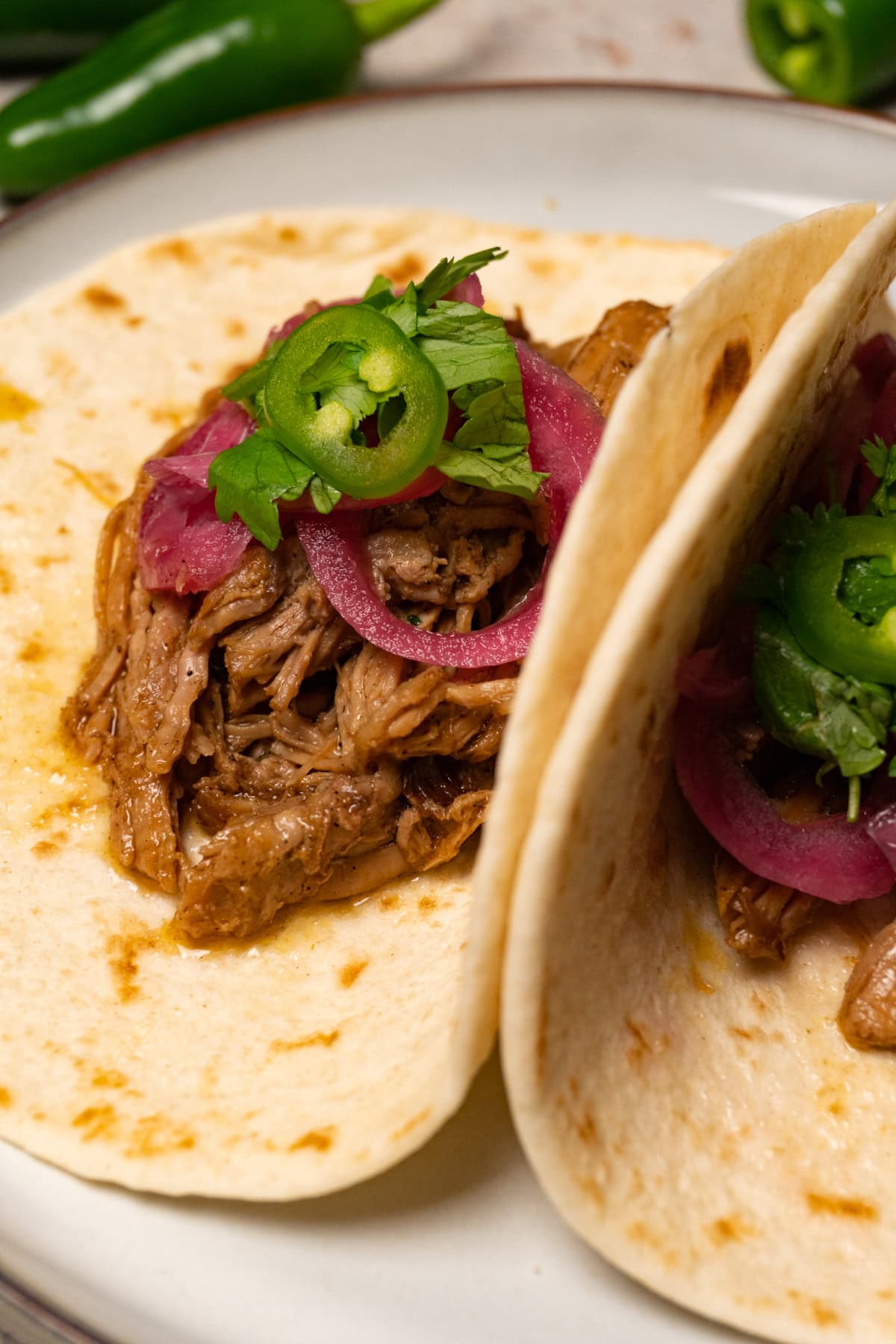 Two taco shells with pulled pork, marinated red onions, fresh cilantro, and jalapeños.