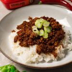 A bowl of rice topped with a generous portion of saucy ground beef and fresh green onions.