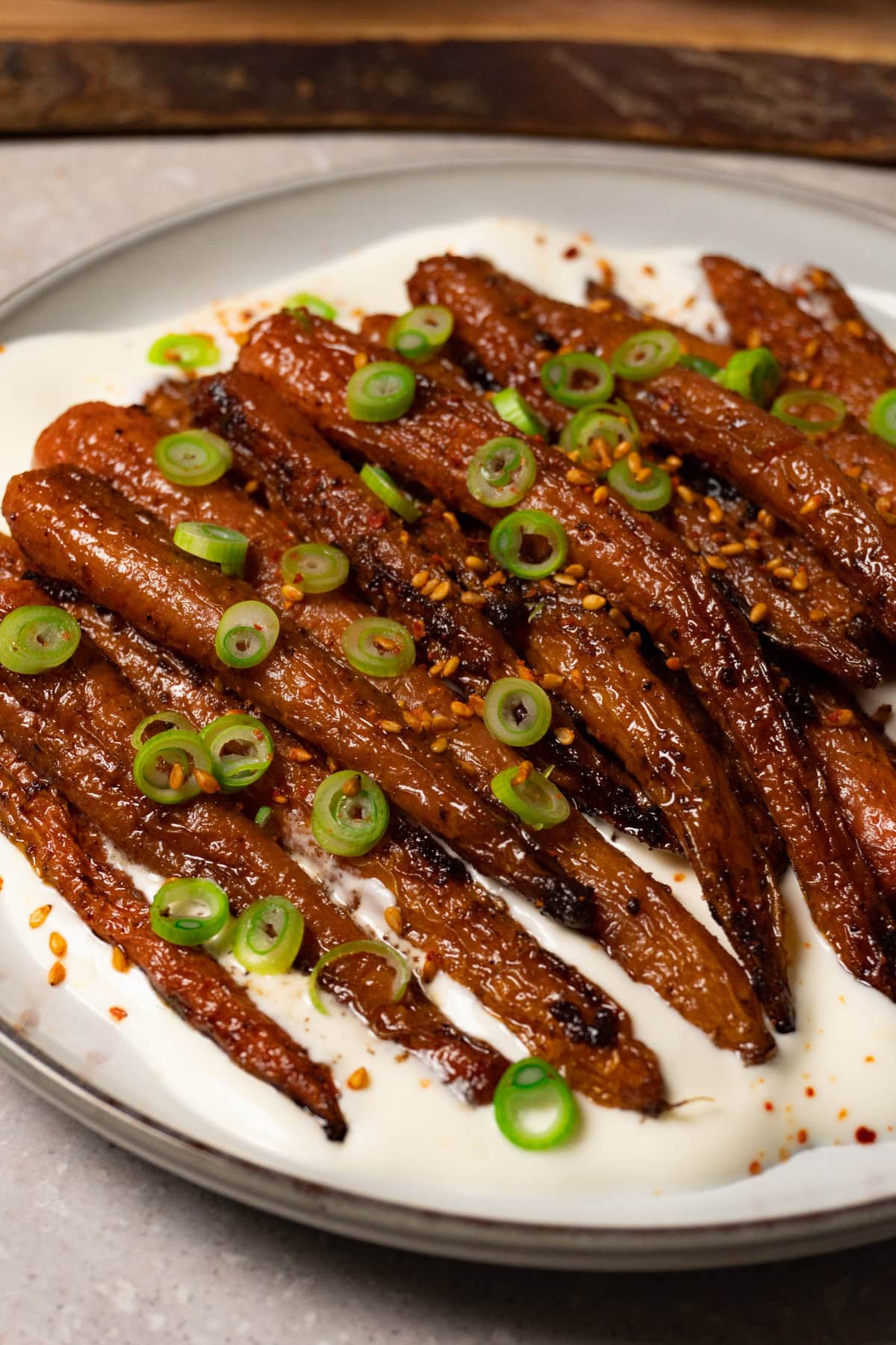 Roasted carrots topped with toasted sesame seeds and green onions, served with white sauce on a plate.