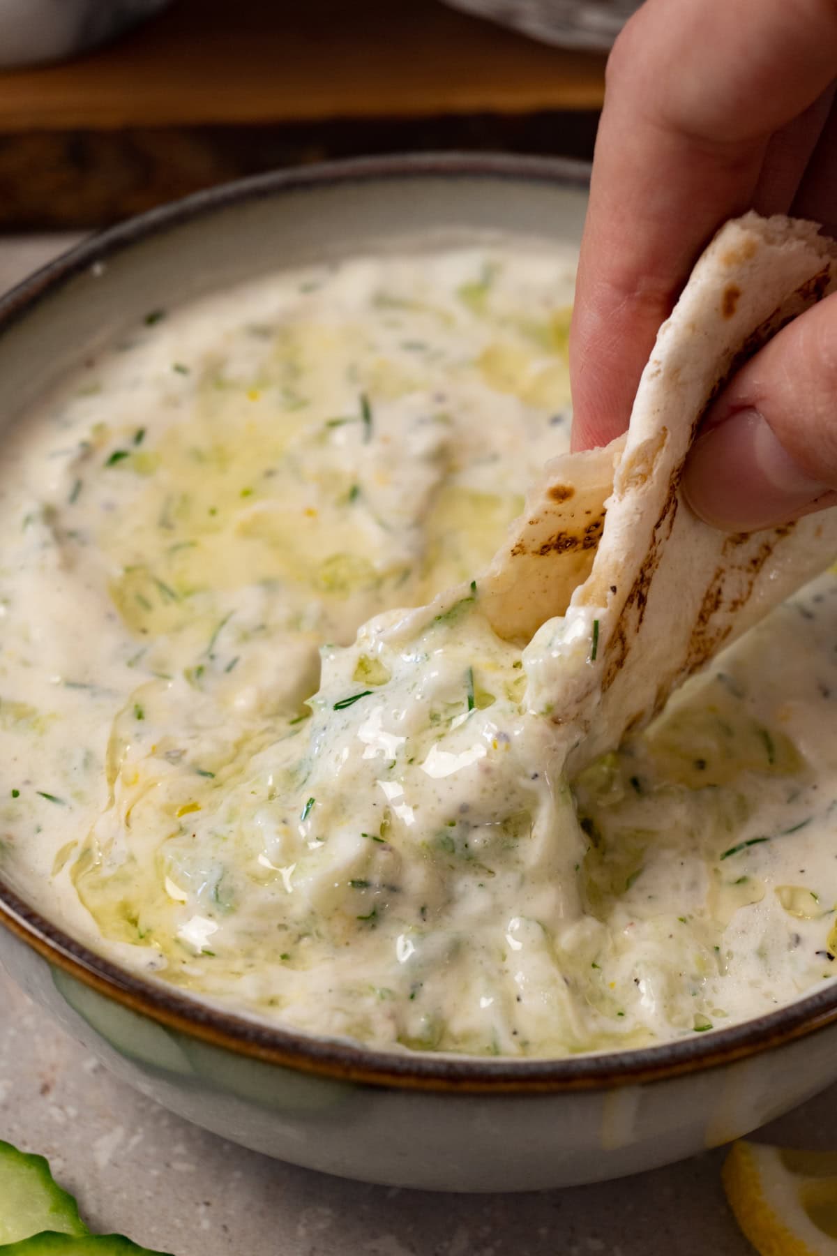 A hand is dipping a piece of flatbread into a bowl of tzatziki sauce.