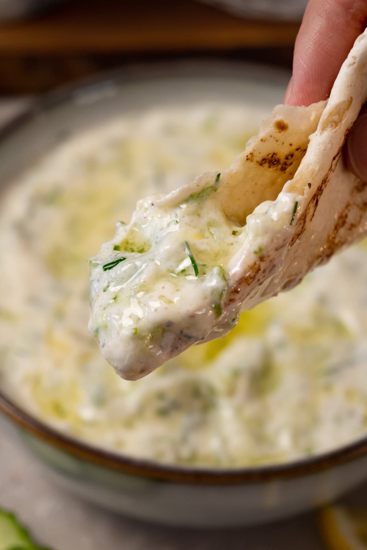 A hand is holding a piece of flatbread with tzatziki sauce.