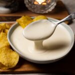 A spoon is scooping white sauce out of a bowl.