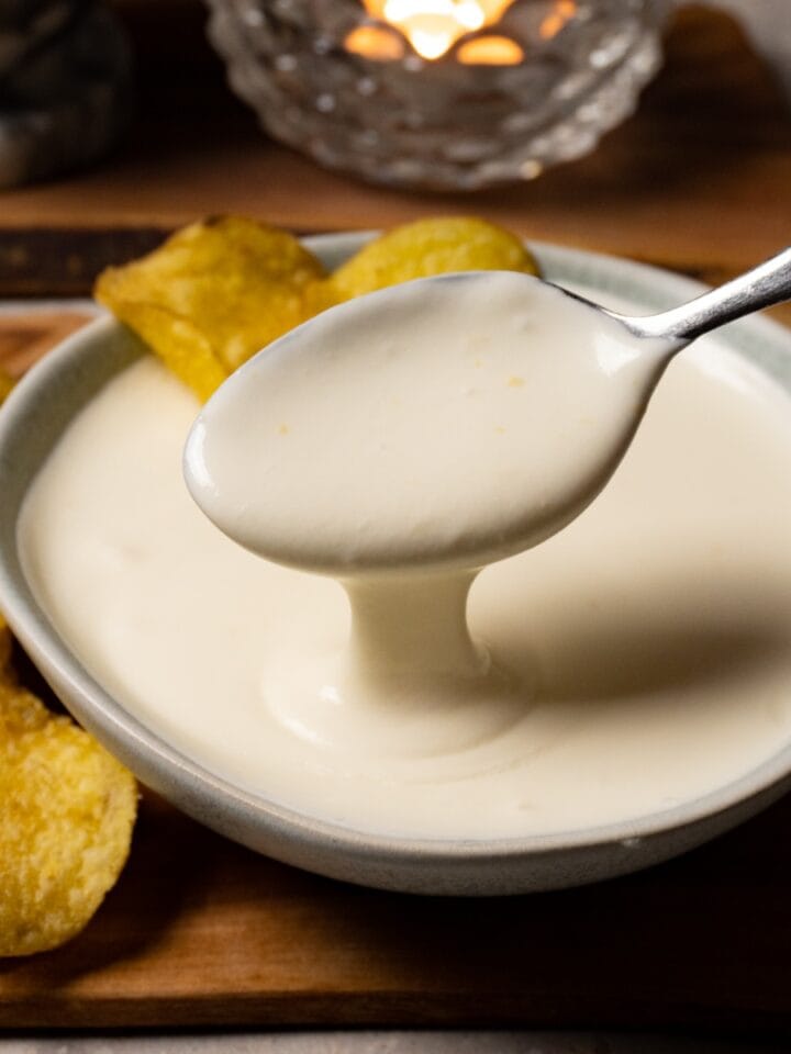 A spoon is scooping white sauce out of a bowl.