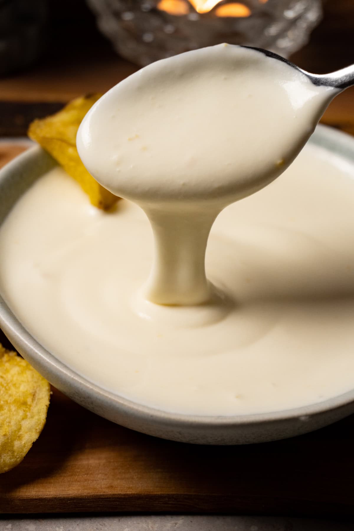 A spoon is scooping white sauce out of a bowl.