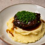 Braised beef cheek is served on top of mashed potatoes and topped with finely chopped chives.