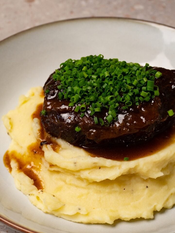 Braised beef cheek is served on top of mashed potatoes and topped with finely chopped chives.
