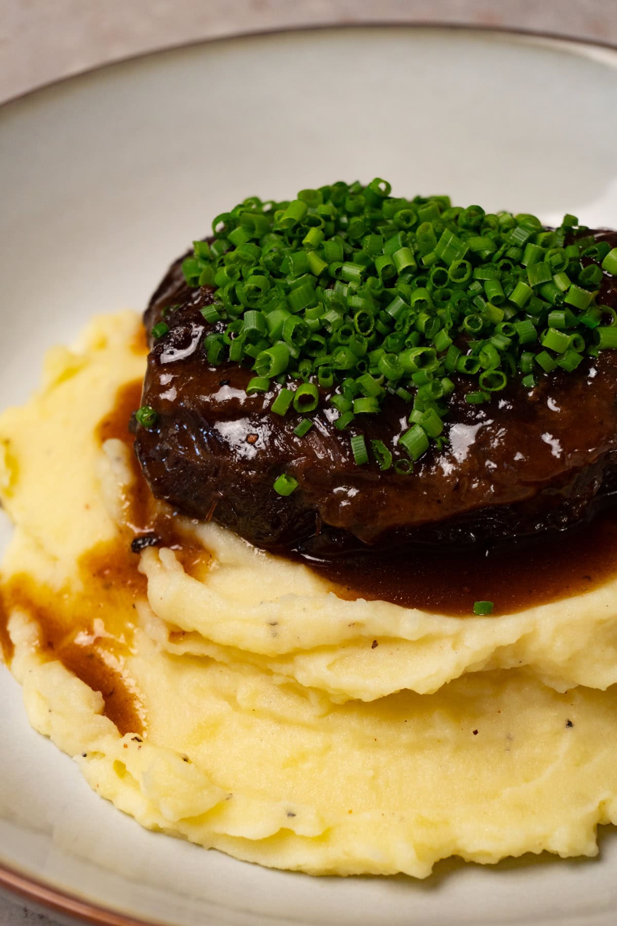 Braised beef cheek is served on top of mashed potatoes and topped with finely chopped chives.