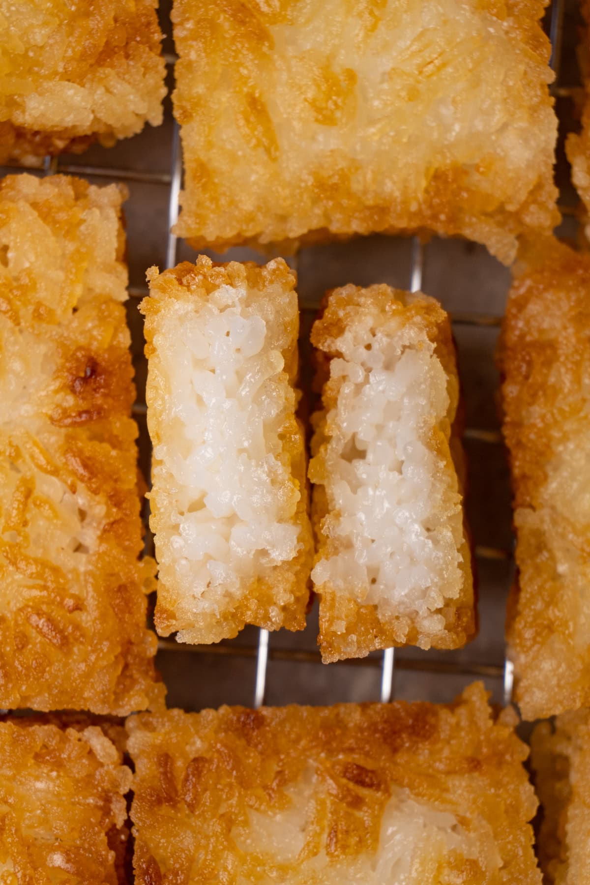 Deep-fried rice cakes on a cooling rack. One cake has been cut in half.