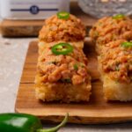 Crispy rice cakes topped with spicy tuna and sliced fresh jalapeños are served on a wooden board.