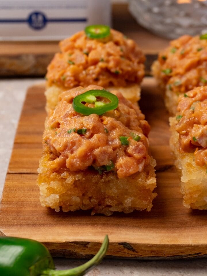 Crispy rice cakes topped with spicy tuna and sliced fresh jalapeños are served on a wooden board.