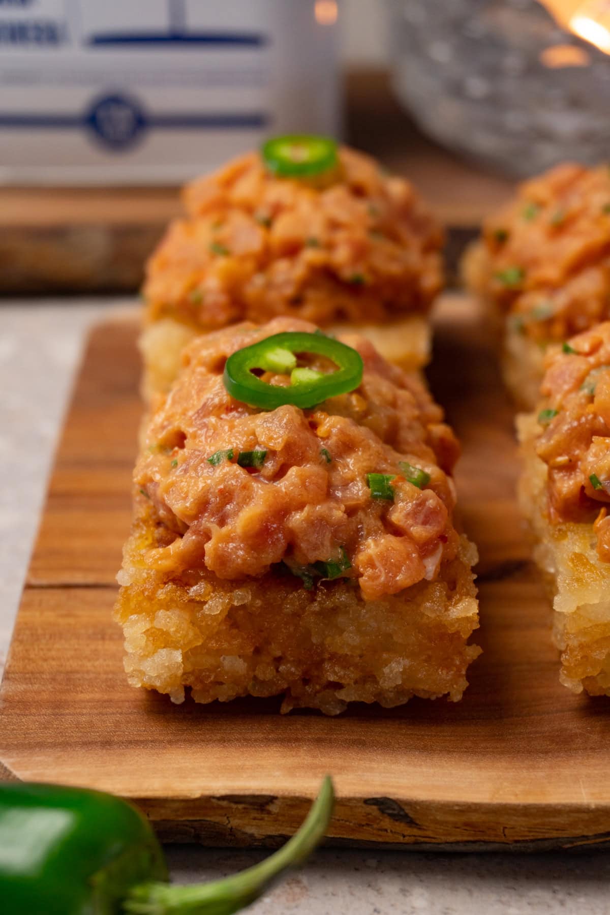 Crispy rice cakes topped with spicy tuna and sliced fresh jalapeños are served on a wooden board.