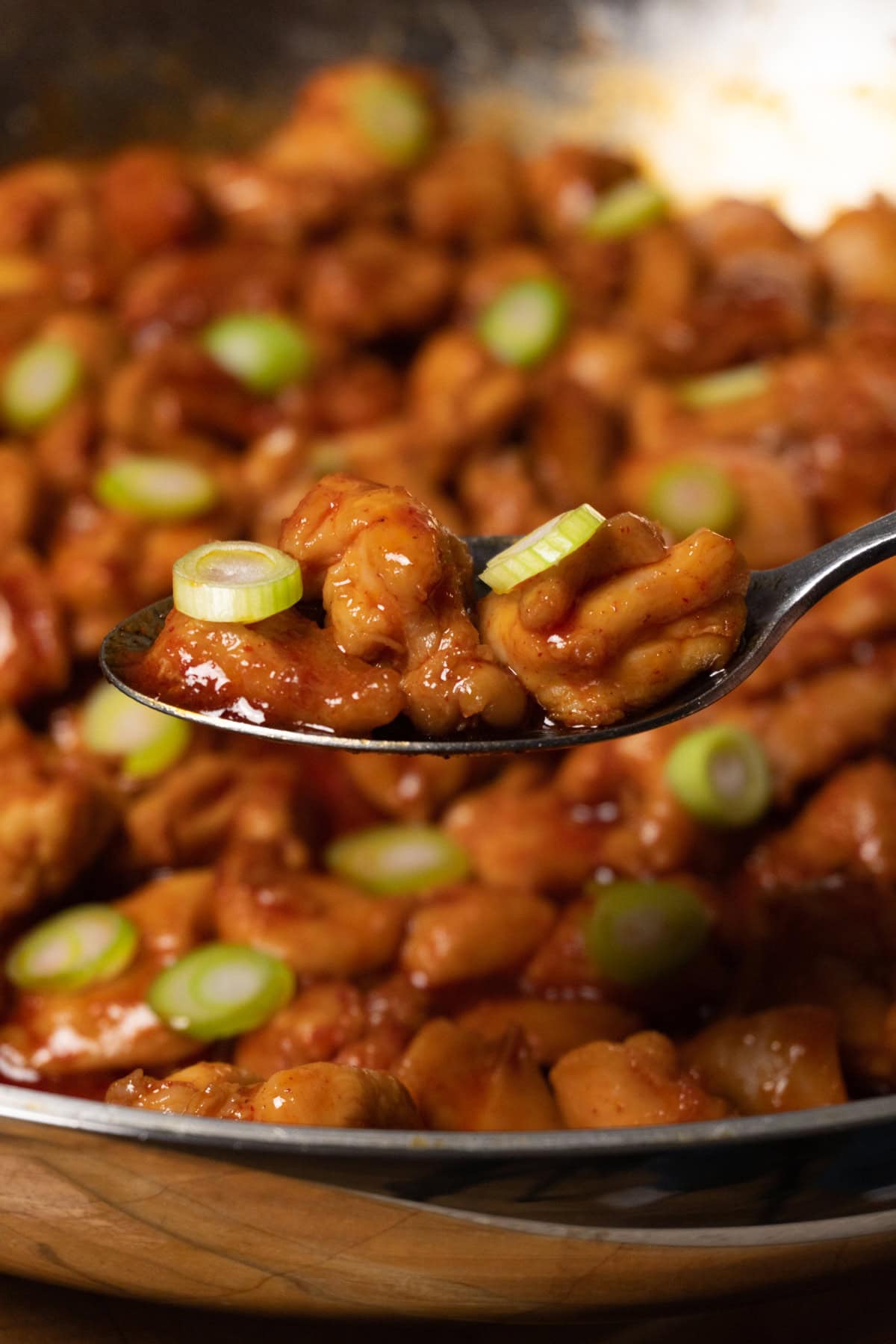 A spoonful of bite-sized chicken covered in red sauce and topped with sliced green onions.