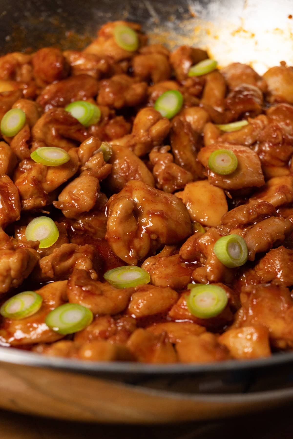 A skillet with bite-sized chicken covered in red sauce and topped with sliced green onions.