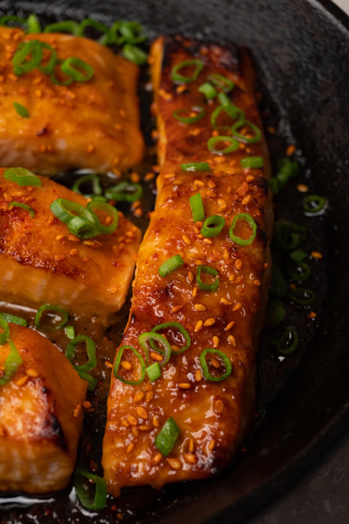 Glazed salmon fillets topped with sesame seeds and green onions in a skillet.