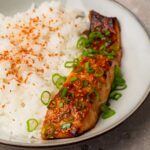 Glazed salmon fillets topped with sesame seeds and green onions in a bowl with jasmine rice on the side.