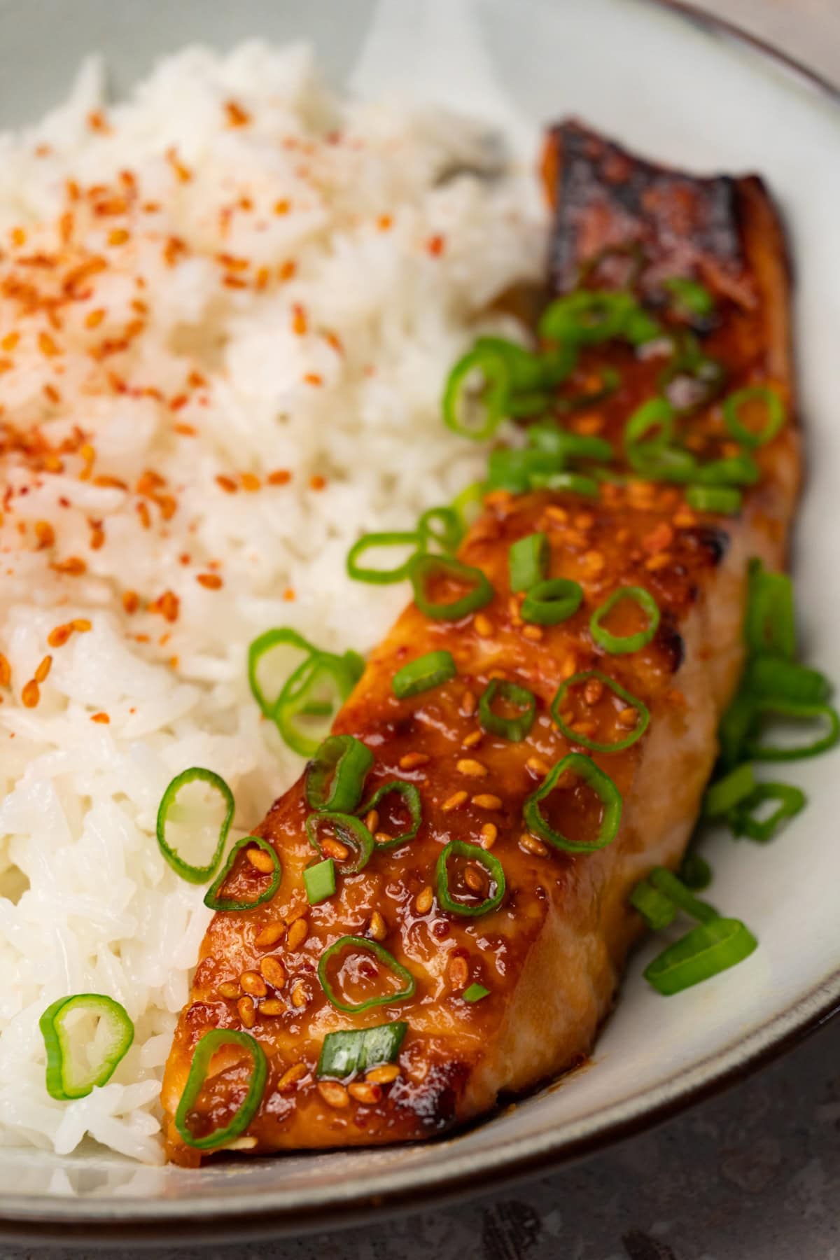 Glazed salmon fillets topped with sesame seeds and green onions in a bowl with jasmine rice on the side.