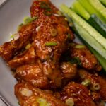 Sticky chicken wings topped with toasted sesame seeds and freshly chopped onion in a bowl.