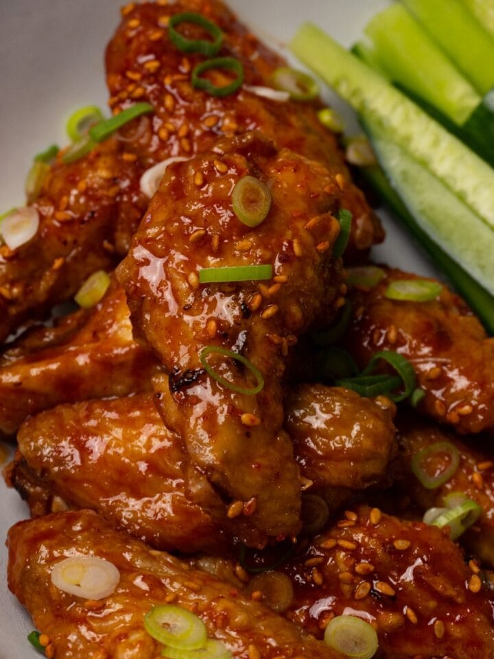 Sticky chicken wings topped with toasted sesame seeds and freshly chopped onion in a bowl.