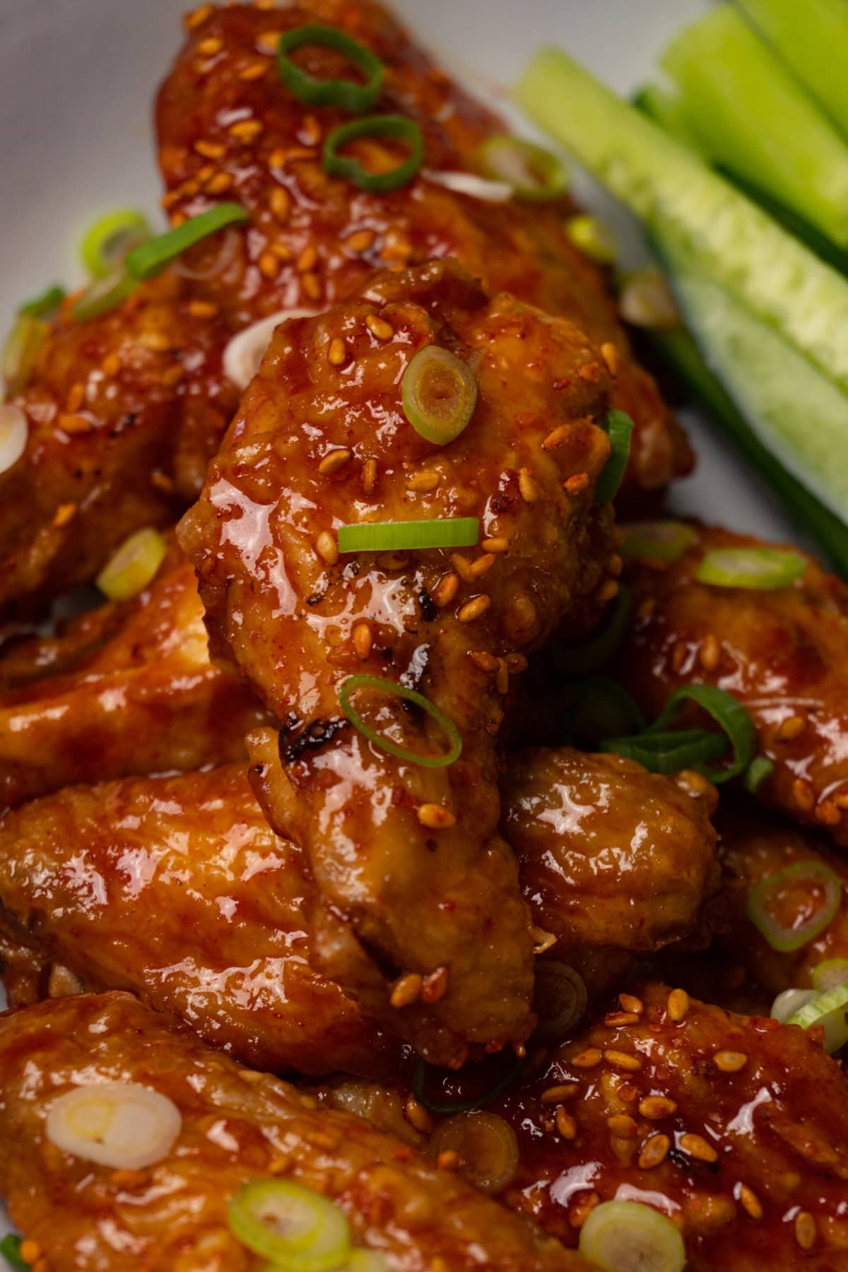 Sticky chicken wings topped with toasted sesame seeds and freshly chopped onion in a bowl.