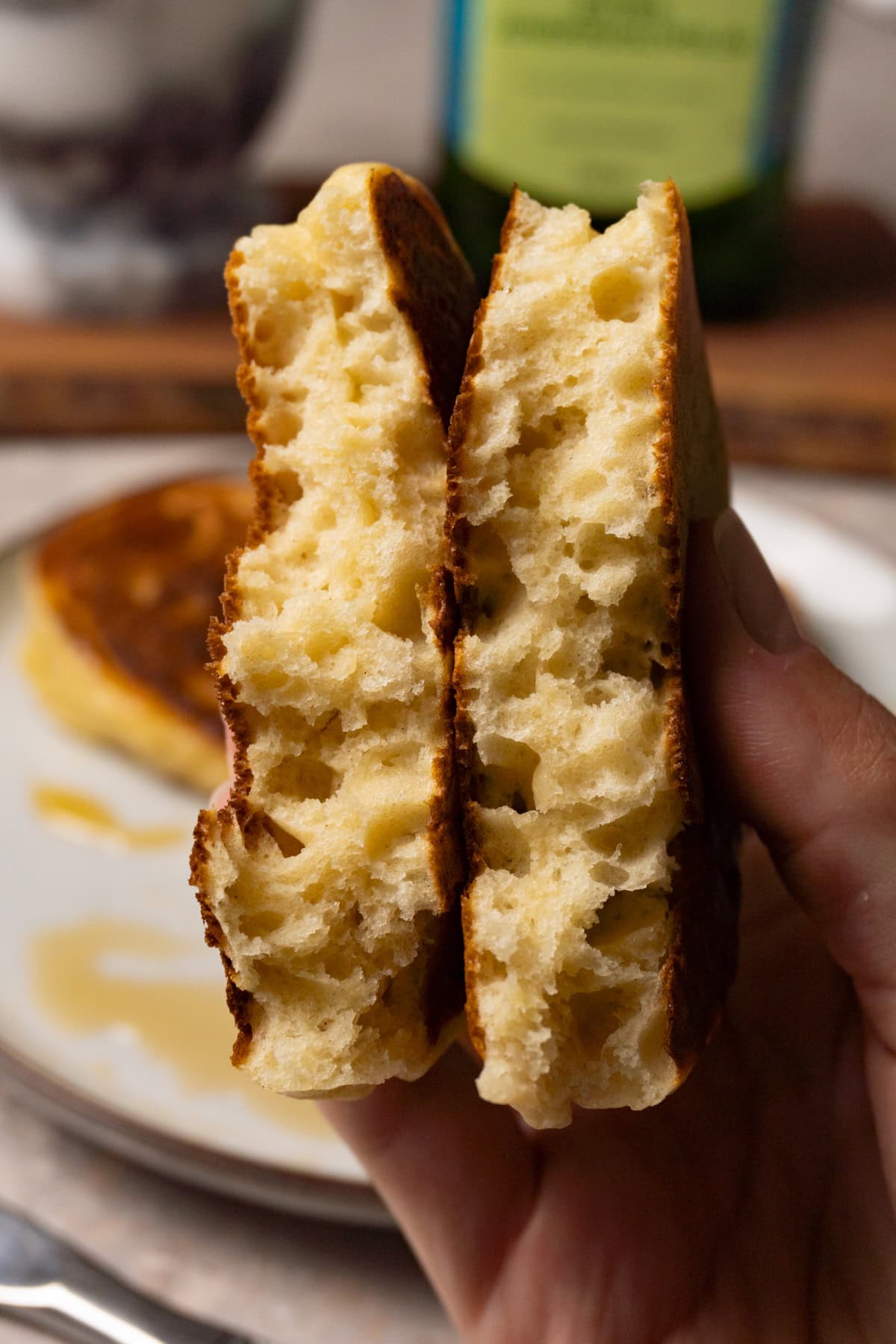 A hand is holding a fluffy pancake ripped in half.