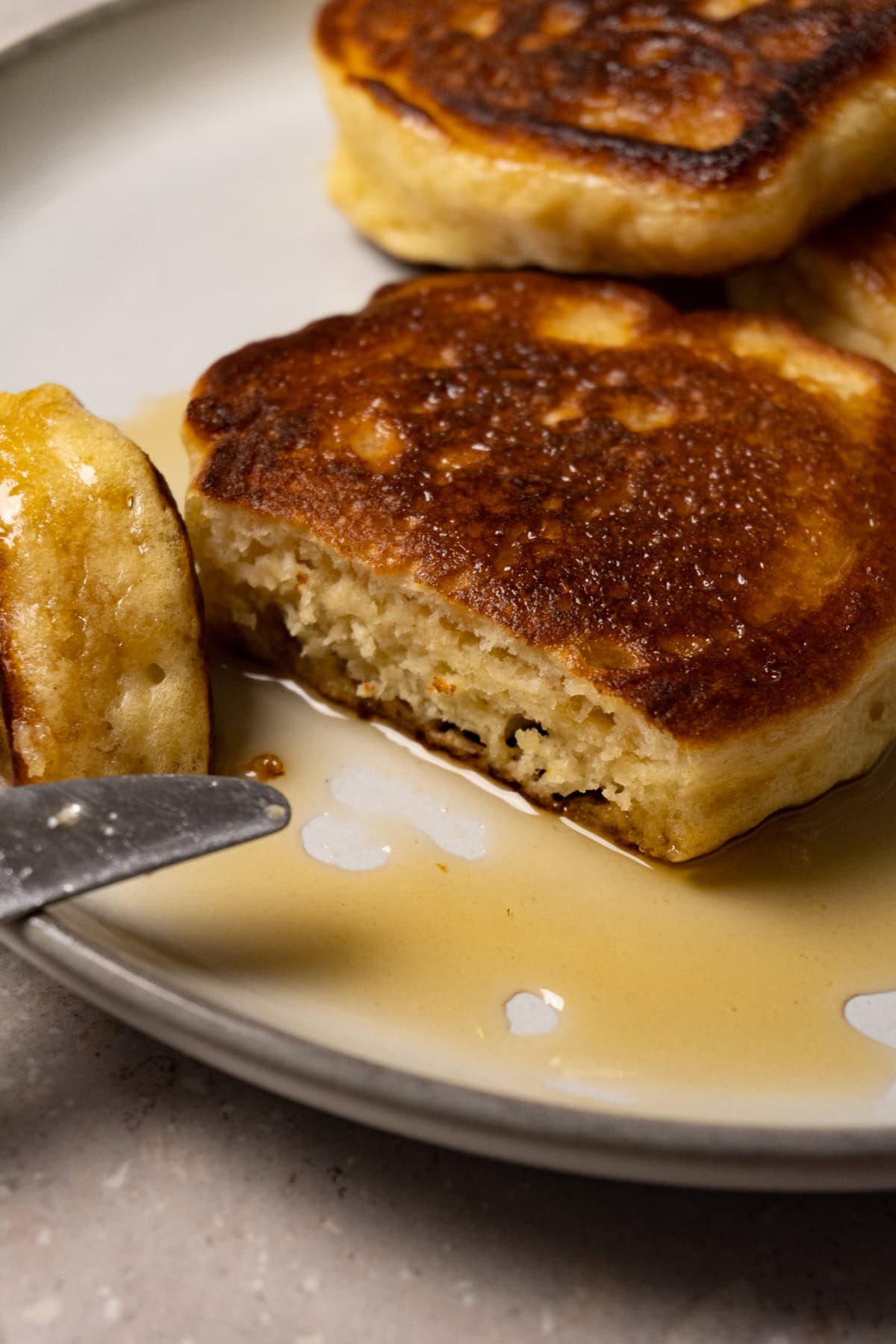Pancakes topped with syrup are served on a plate. A piece has been cut from one of the pancakes.