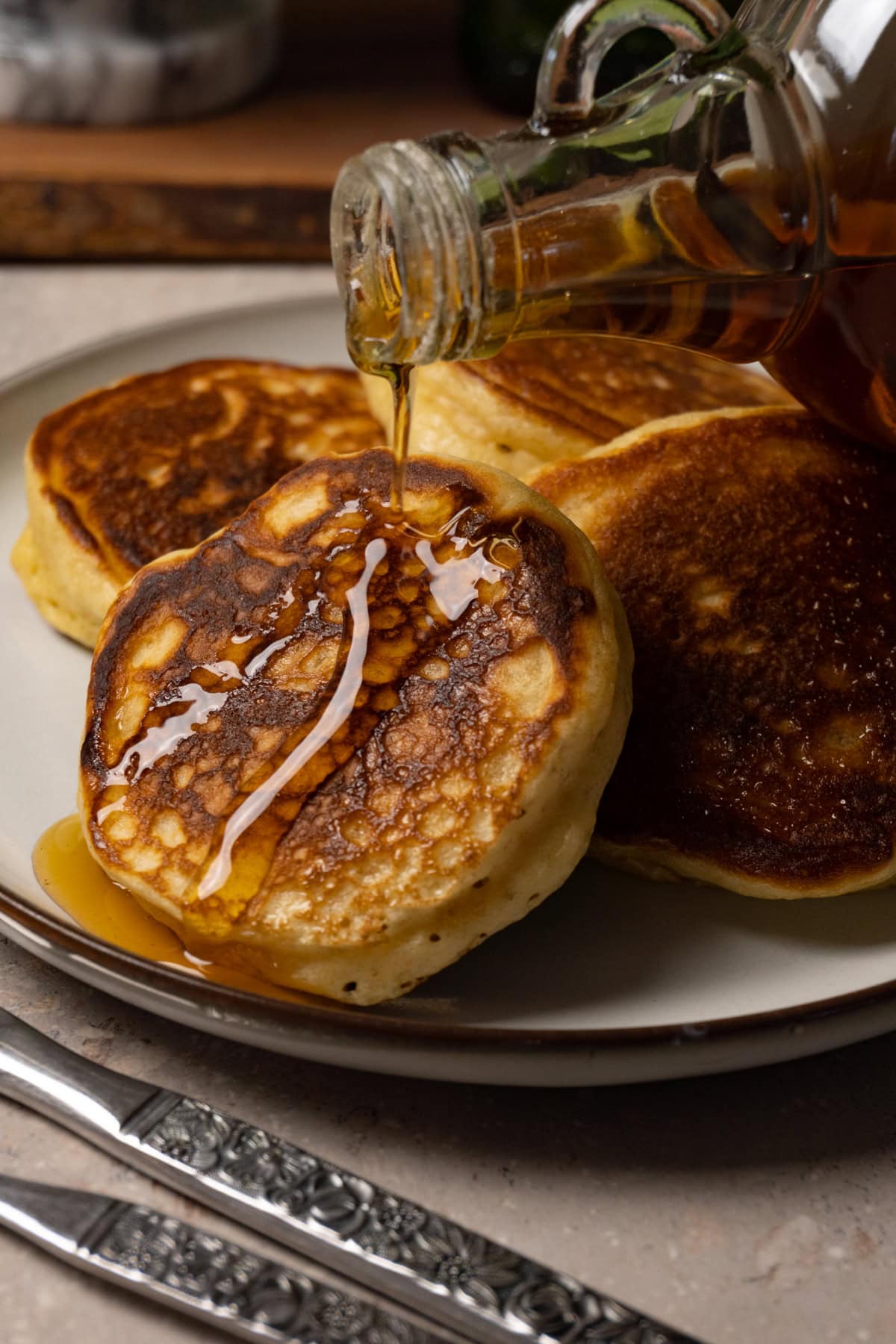 Pancakes served on a plate are being topped with maple syrup.