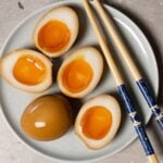 Halved ramen eggs served on a plate with chopsticks.