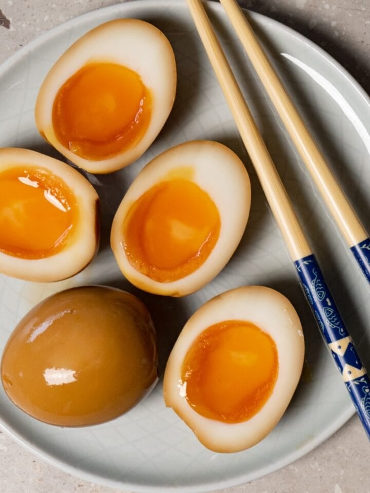 Halved ramen eggs served on a plate with chopsticks.