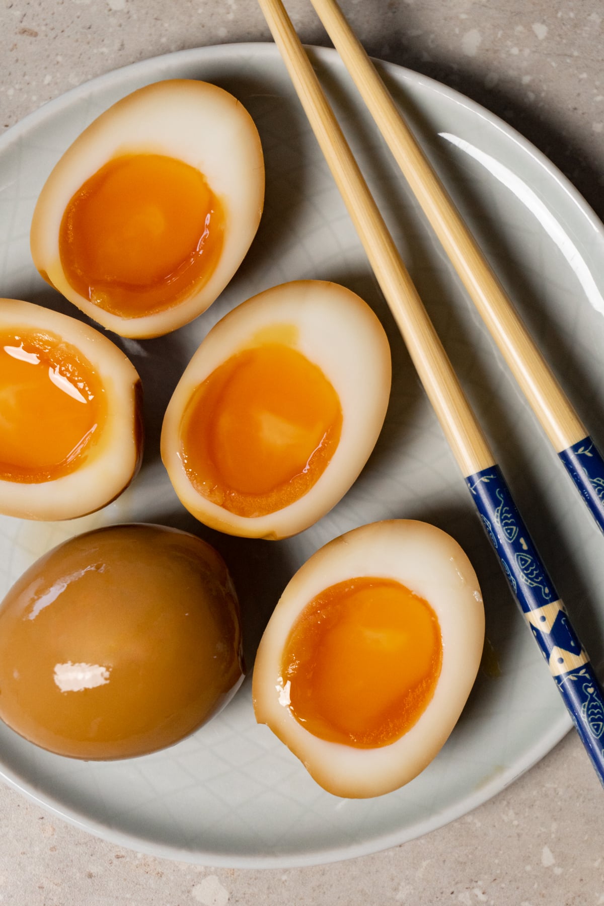 Halved ramen eggs served on a plate with chopsticks.