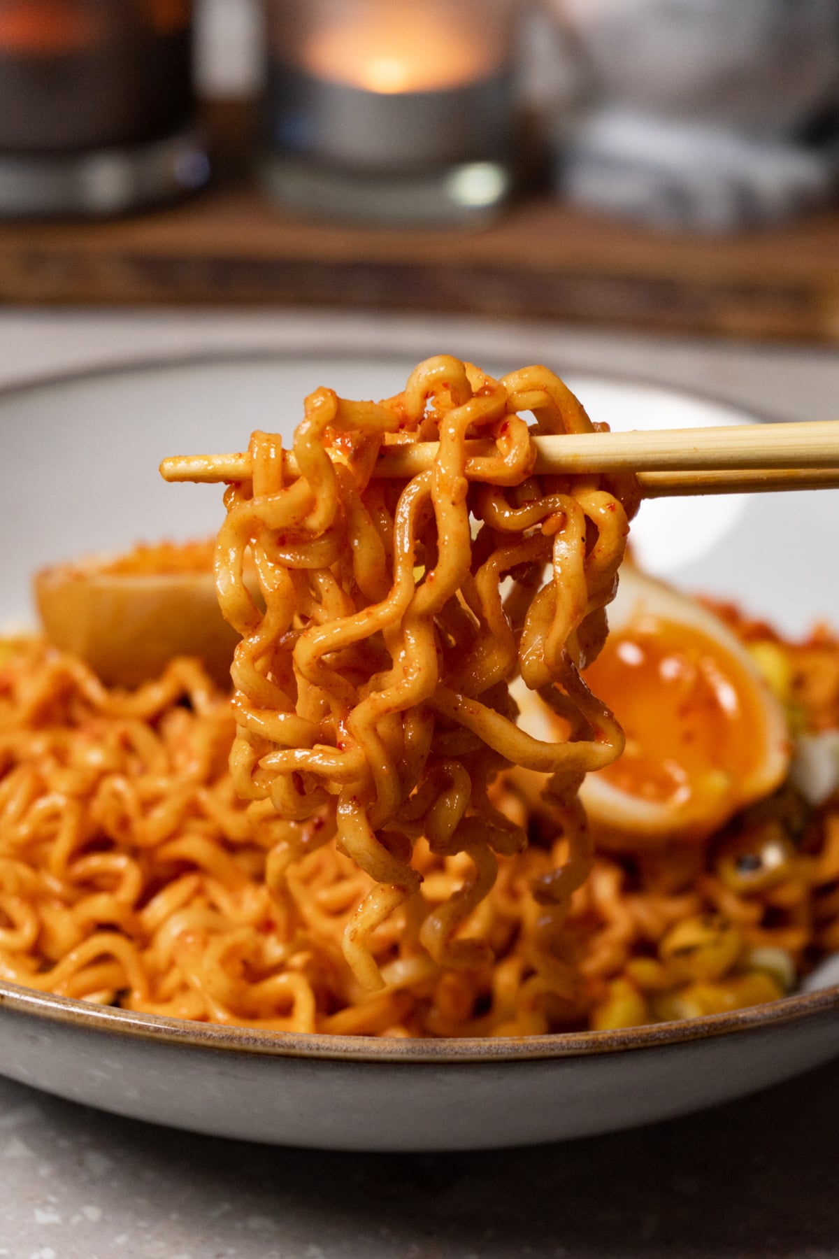 Chopsticks holding ramen noodles covered in red sauce.
